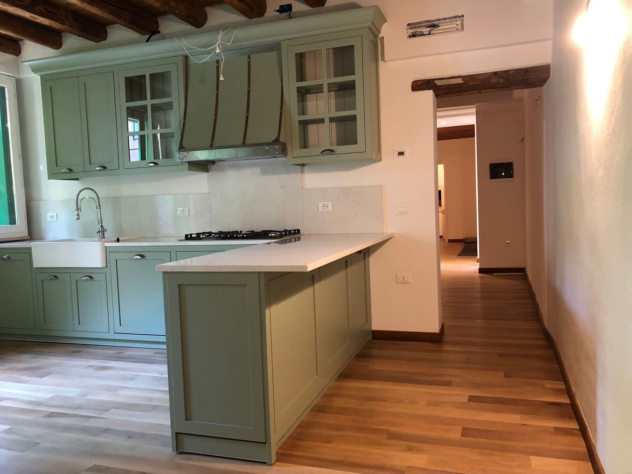 Cucina su misura a Vicenza con isola laccata verde salvia, piano chiaro e soffitto con travi in legno