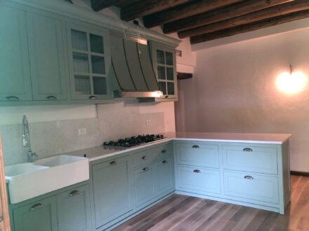 Cucina su misura a Vicenza con ante laccate verde salvia, isola contenitiva e soffitto con travi in legno a vista