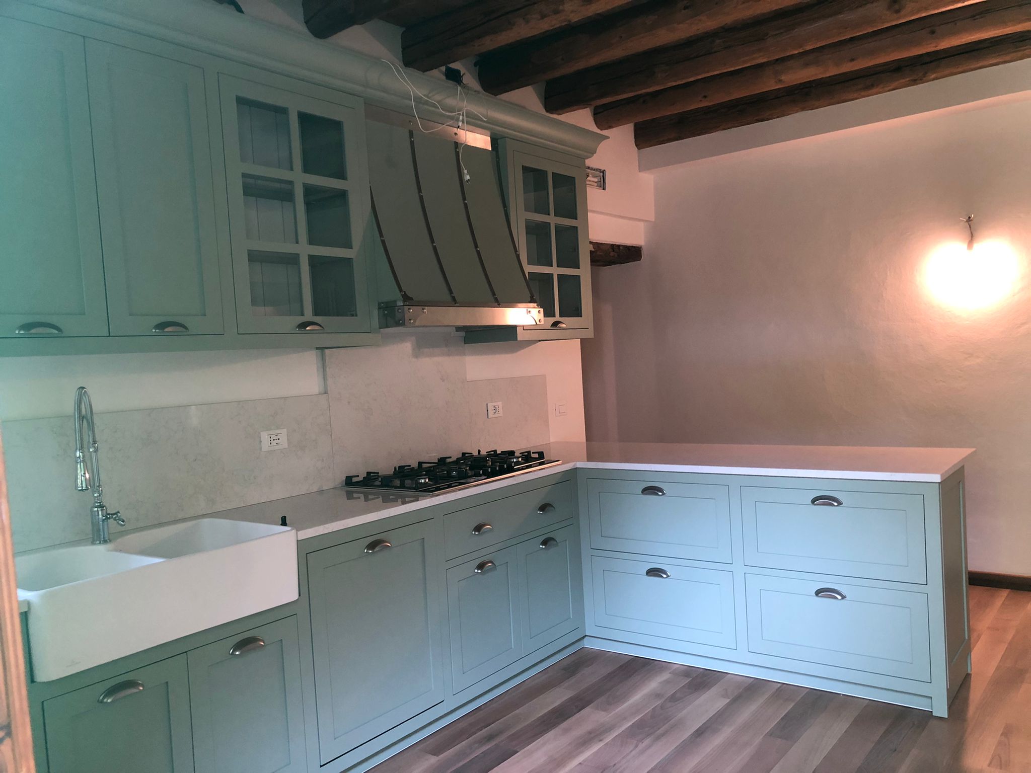 Cucina su misura a Vicenza con ante laccate verde salvia, isola contenitiva e soffitto con travi in legno a vista