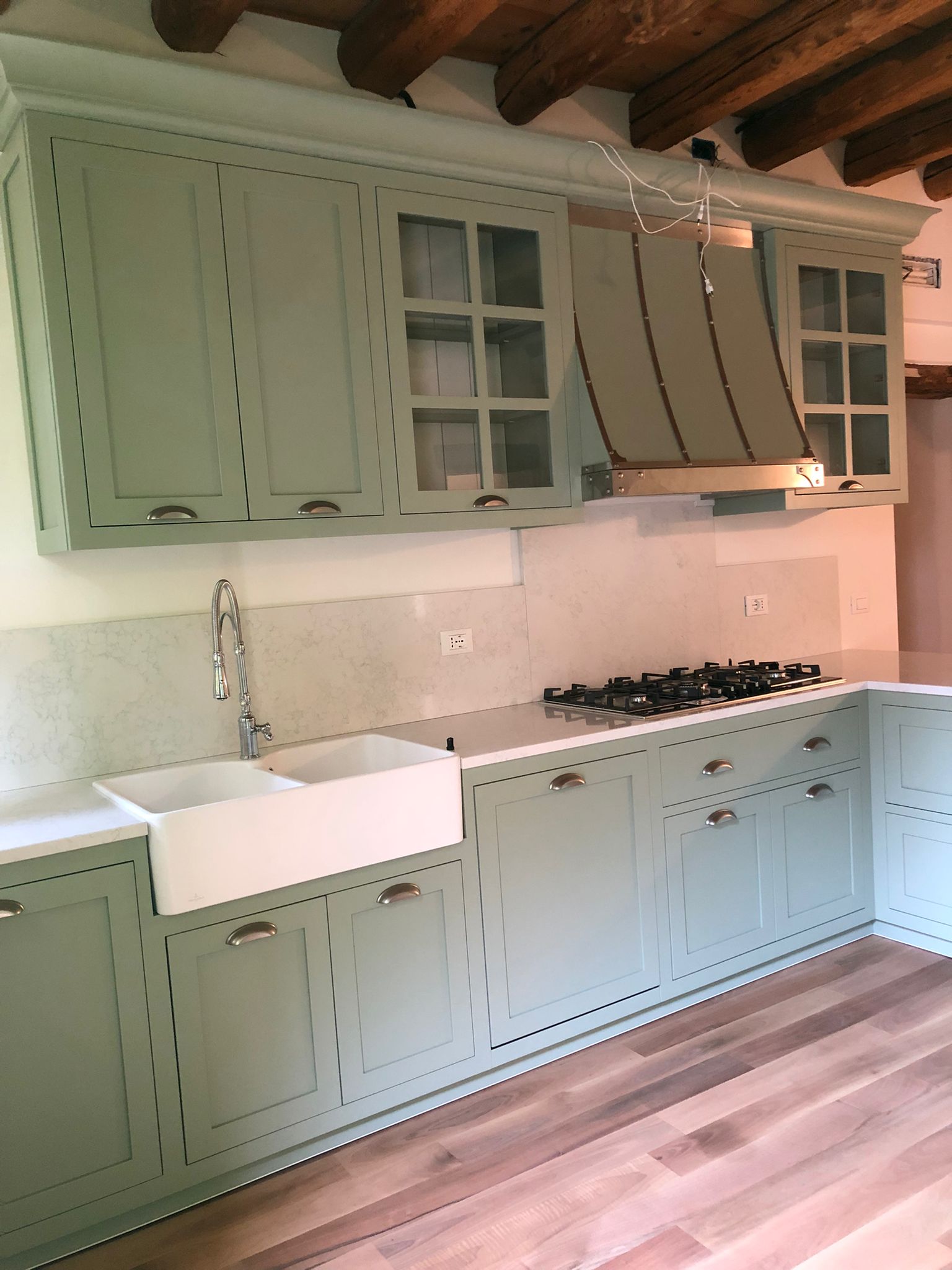 Cucina su misura a Vicenza con ante classiche laccate verde salvia, lavello farmhouse e travi in legno a vista