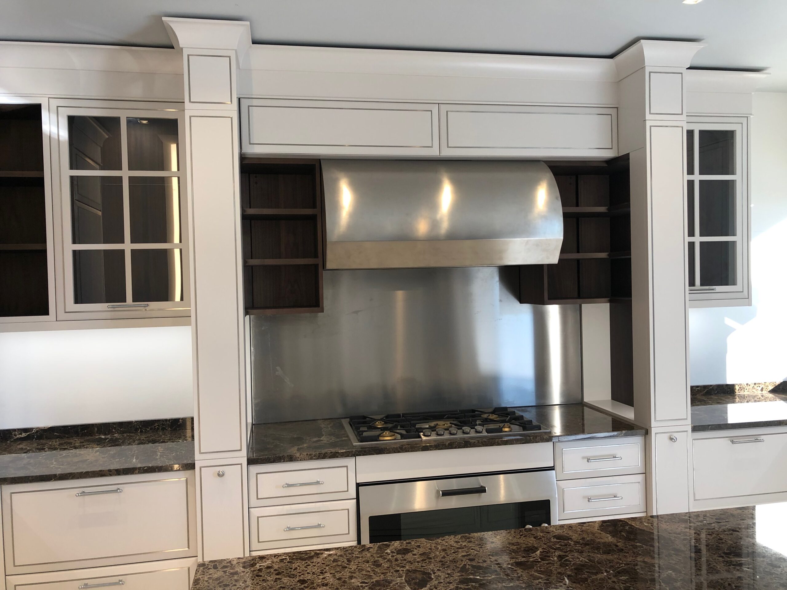 Zona cottura di cucina su misura a Piacenza con piano a gas, cappa in acciaio e mobili classici laccati, realizzata da Martini Verona